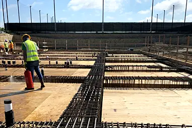 A crew member in a hard hat and high-vis vest working on a rebar layout